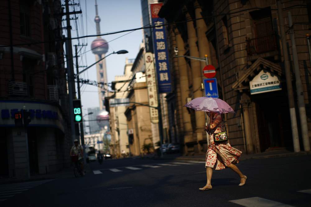 A&amp;nbsp;woman uses an umbrella to protect herself from the sun as she crosses a busy street in downtown Shanghai, August 6, 2013. REUTERS\/Carlos Barria